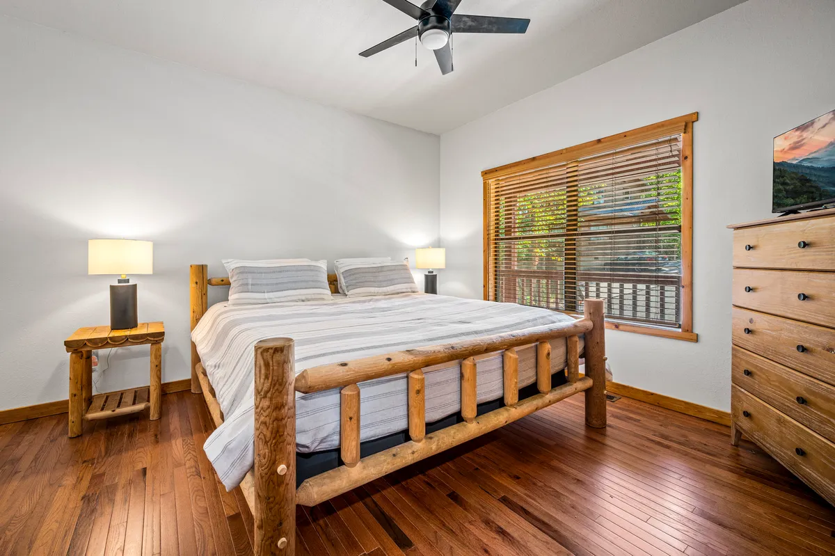 A tranquil bedroom with a sturdy wooden bed frame, ample natural light streaming in through a window, and stylish decorative lamps. The overall mood is calm and restful, ideal for recharging.