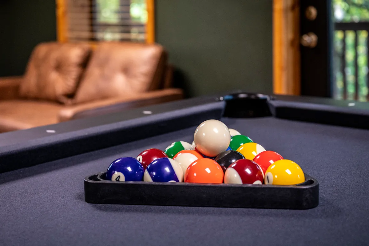 Inside, a pool table takes center stage in a cozy game room furnished with a leather couch. Arranged billiard balls and the inviting seating create an atmosphere of friendly competition and shared fun for larger groups.