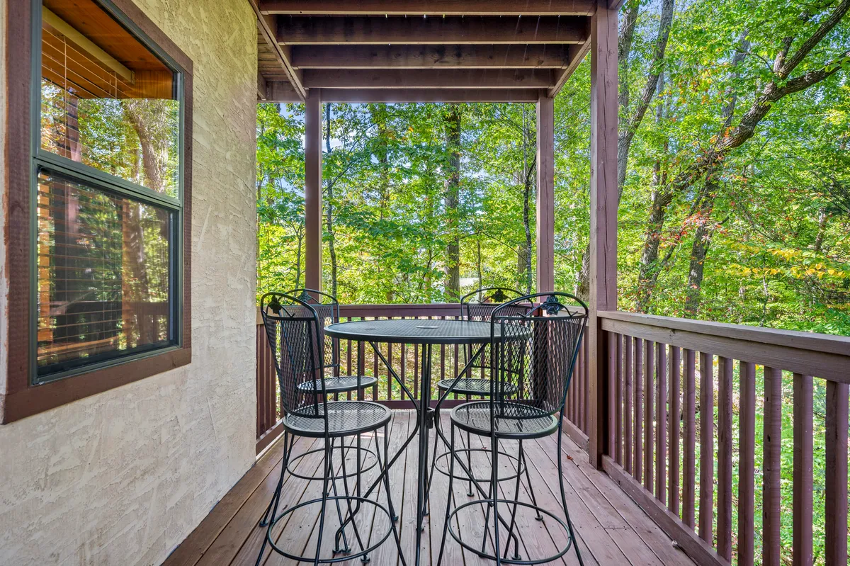 A cozy exterior deck scene featuring a bistro table and black metal chairs surrounded by lush greenery. The deck, bathed in soft natural light, exudes peacefulness and invites guests to enjoy morning coffee or unwind after a day of adventure.