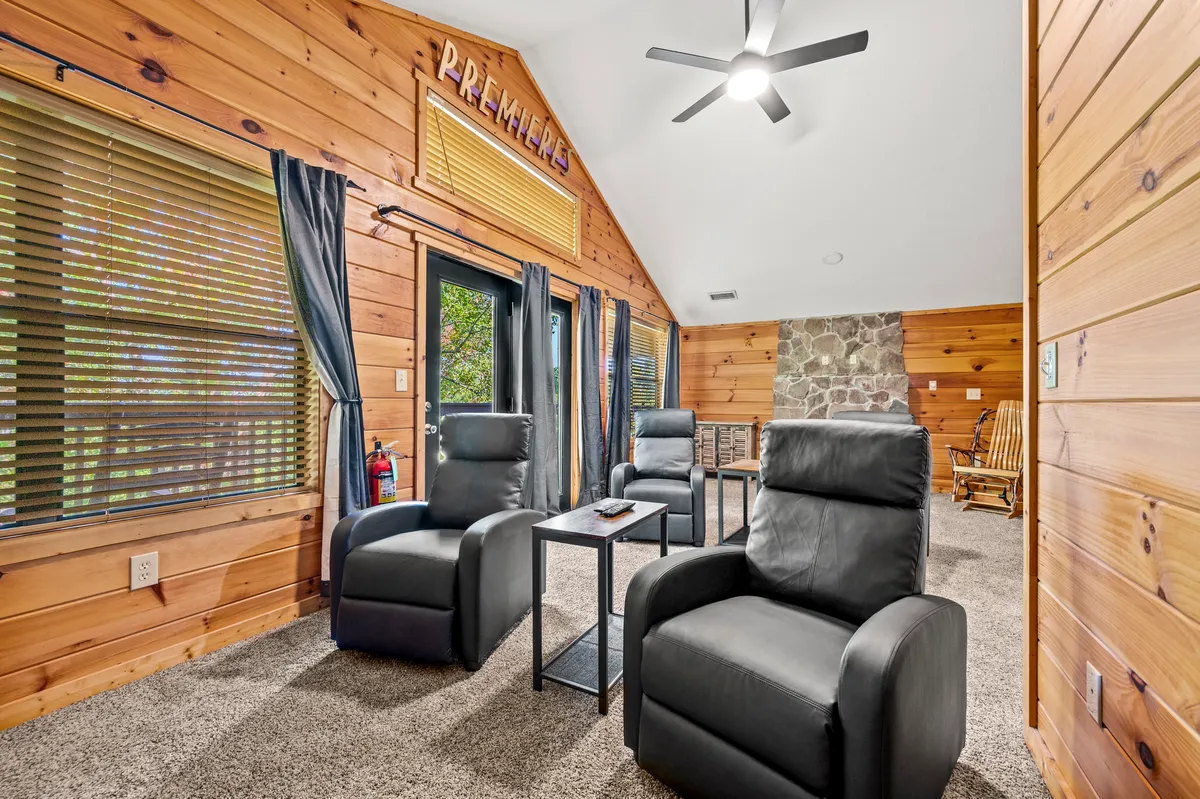 A cozy movie theater room with rows of reclining chairs facing a feature wall, large windows letting in daylight, and a warm, comfortable atmosphere. The space invites families to unwind together with a movie night after busy days out.