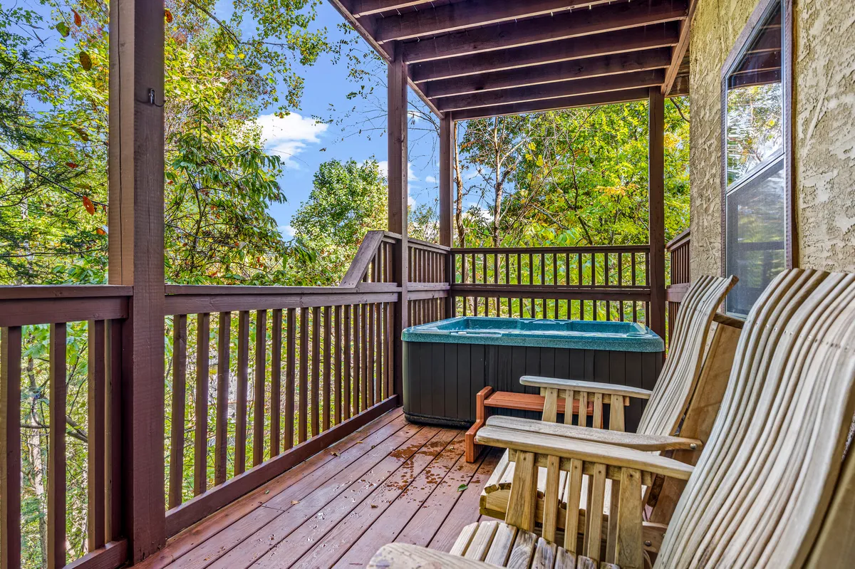 A bubbling hot tub sits on a wooden deck, flanked by wooden chairs and surrounded by tall trees, with soft sunlight filtering through. The scene exudes relaxation, inviting guests to unwind while immersed in nature.