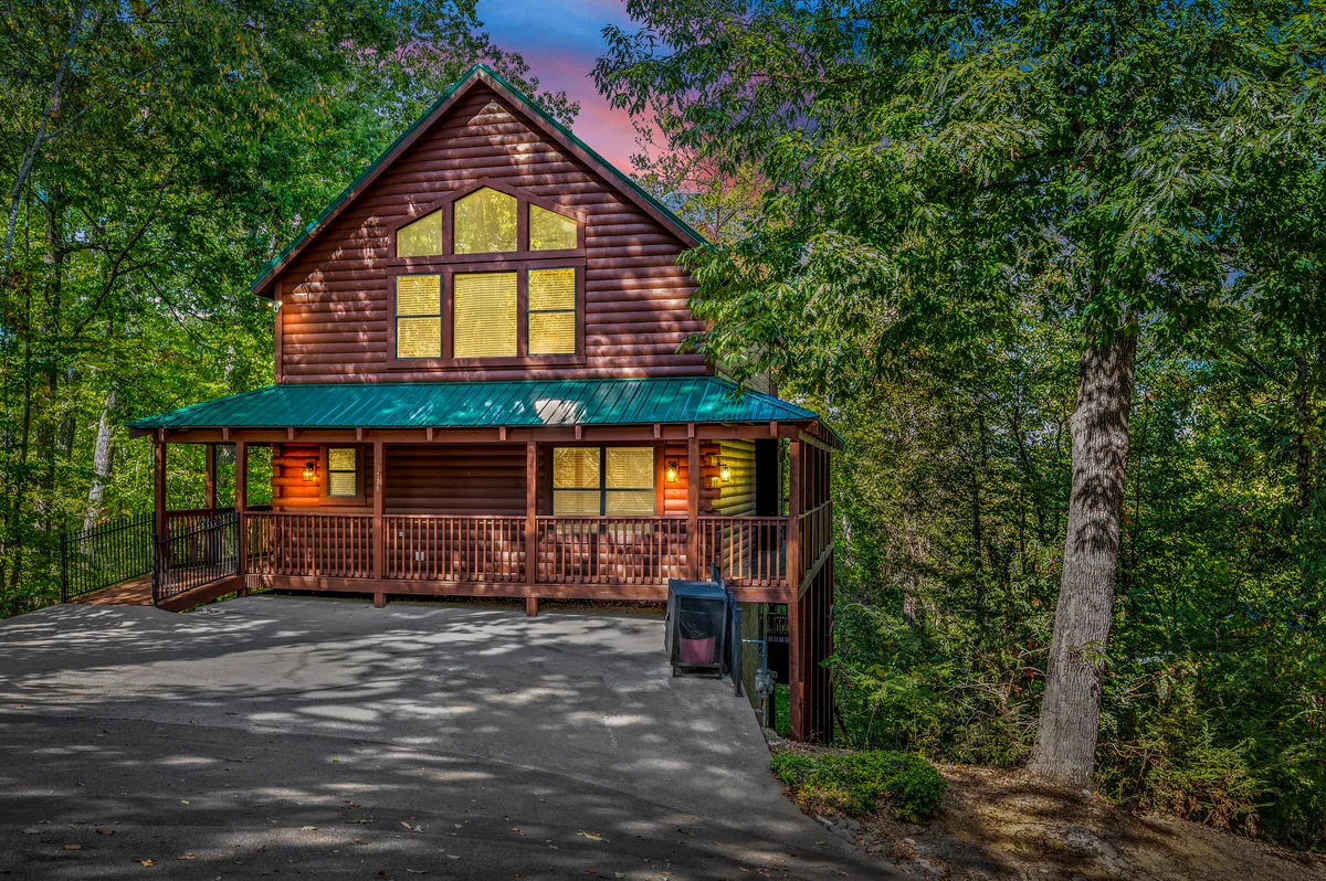 This exterior image showcases a welcoming wooden structure with large windows surrounded by greenery. The porch with railing hints at a cozy gathering place for guests to relax, share stories, or enjoy the fresh mountain air. The overall atmosphere is tranquil and inclusive, encouraging both relaxation and togetherness.