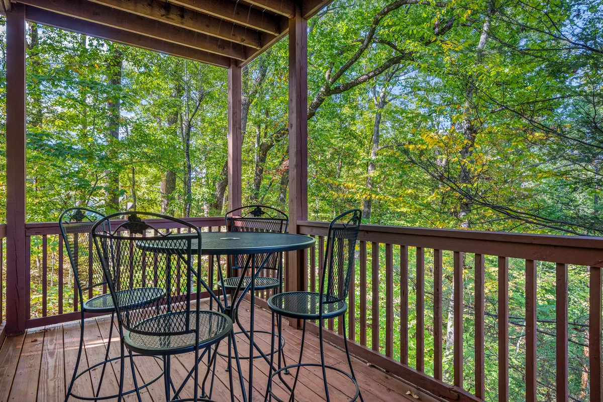 This image features an outdoor dining table set on a deck, encircled by trees and bordered by a wooden railing. The inviting scene is ideal for enjoying meals outdoors while taking in the natural surroundings.