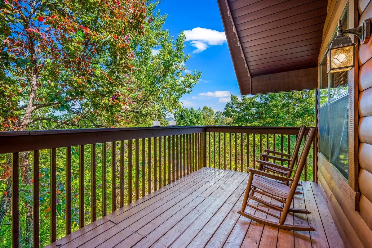 This image depicts a pair of classic wooden rocking chairs on a private deck, surrounded by lush greenery and distant trees. The serene environment suggests peaceful moments spent relaxing or reading outdoors, with the possibility of catching sunset views and wildlife sightings.