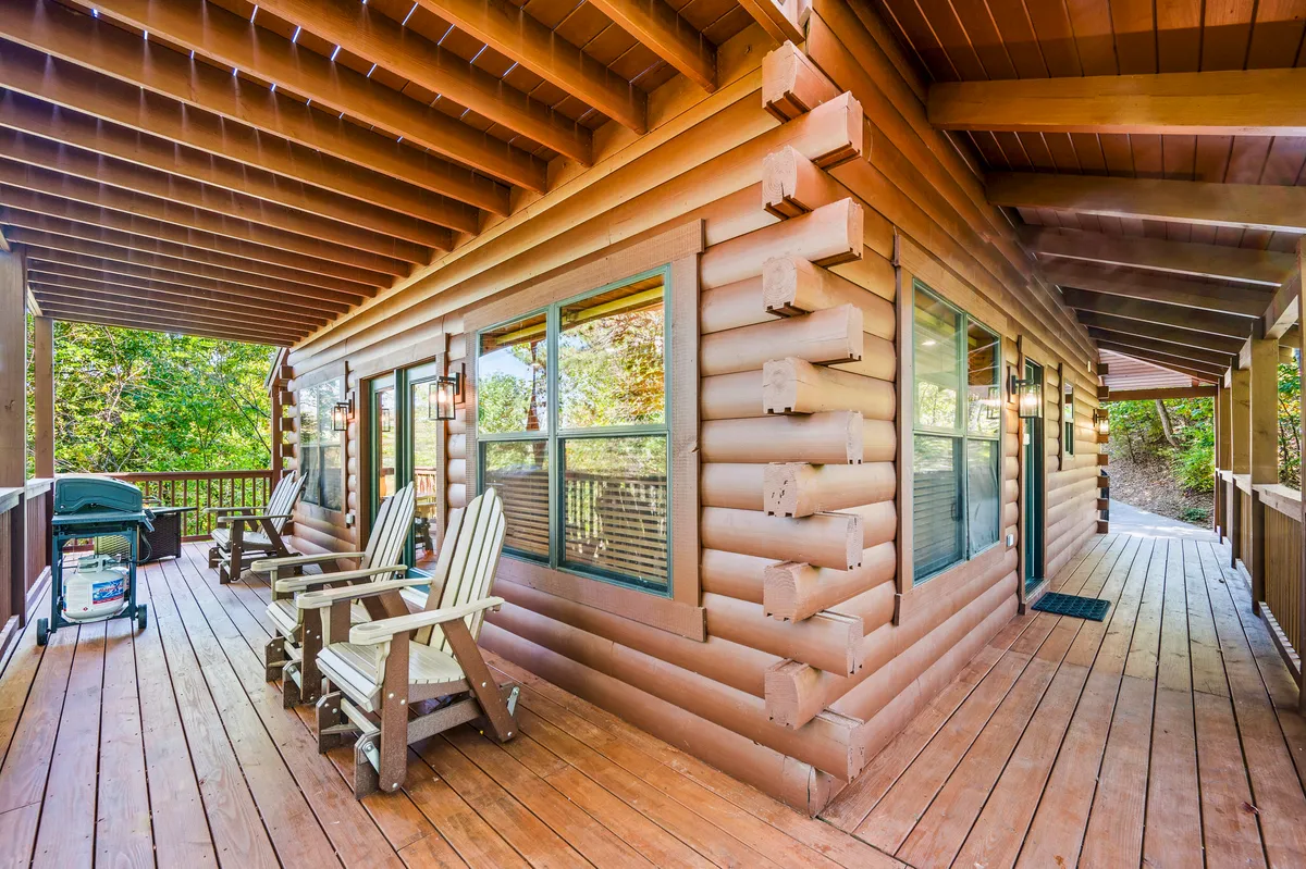 This image captures the cabin's log structure with a spacious wooden deck and adirondack chairs set against a backdrop of lush green foliage. The deck is perfect for outdoor gatherings, showcasing a relaxed, social atmosphere and the seamless connection between indoor comfort and outdoor adventure.